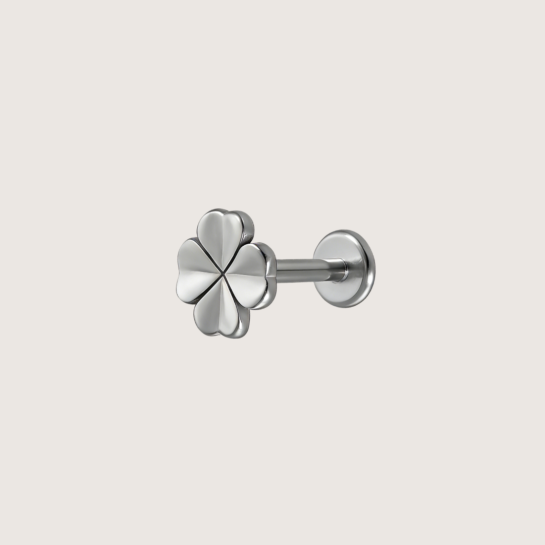 A silver four-leaf clover stud earring with a polished finish, shown from a three-quarter angle on a light beige background.