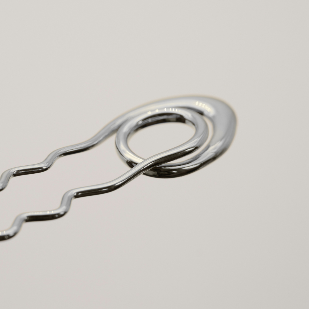 A close-up of a shiny silver metal bobby pin on a light gray background.