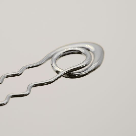 A close-up of a shiny silver metal bobby pin on a light gray background.