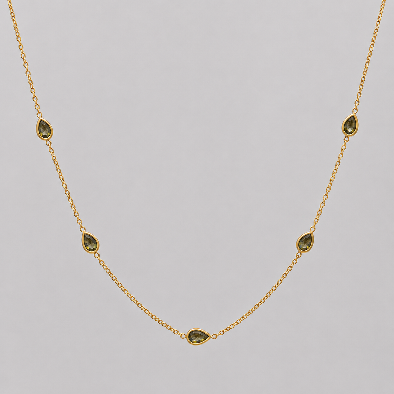 Gold necklace with green gemstones on a grey background
