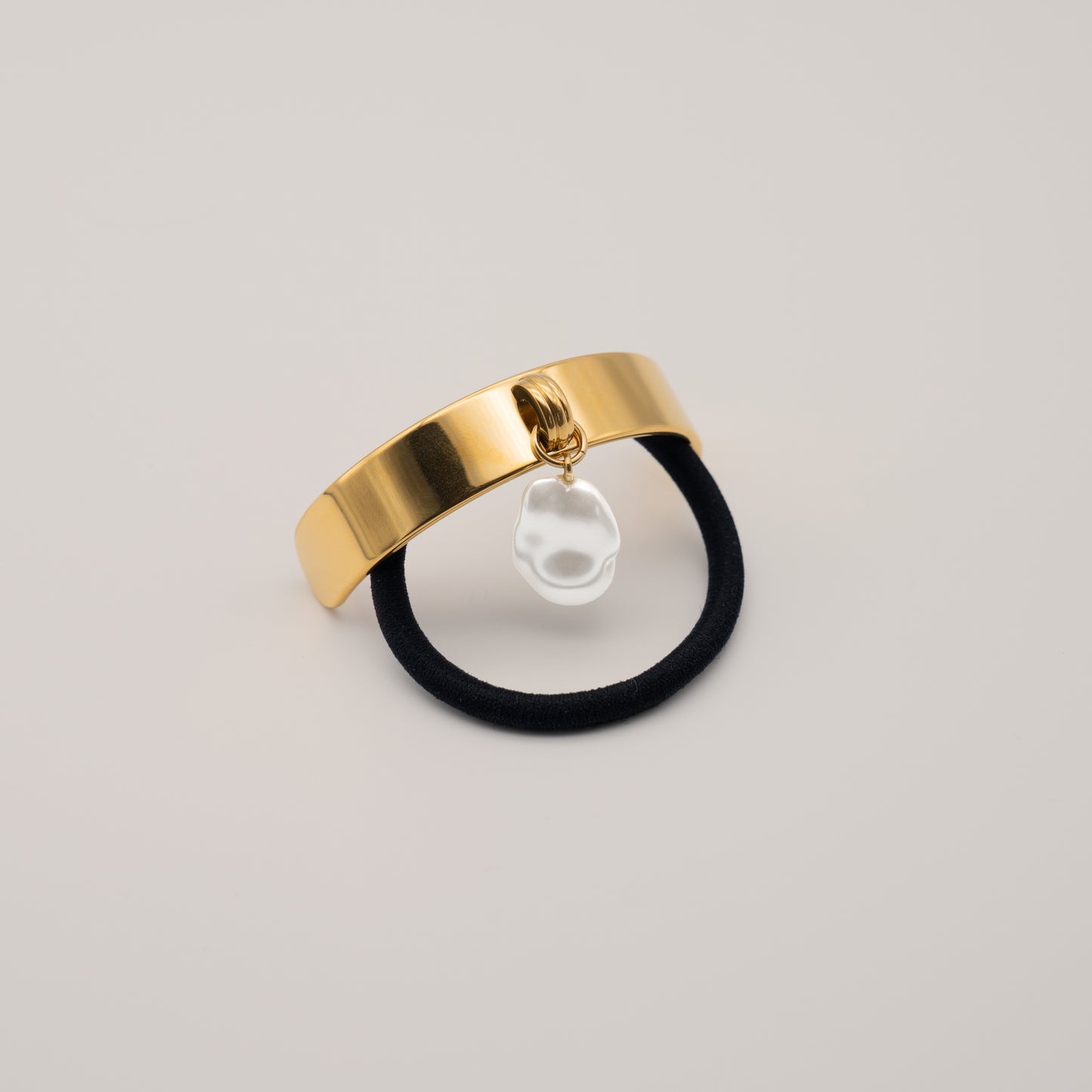 Flat lay of Rosy Collective gold ponytail hair cuff with a freshwater pearl hair accessories