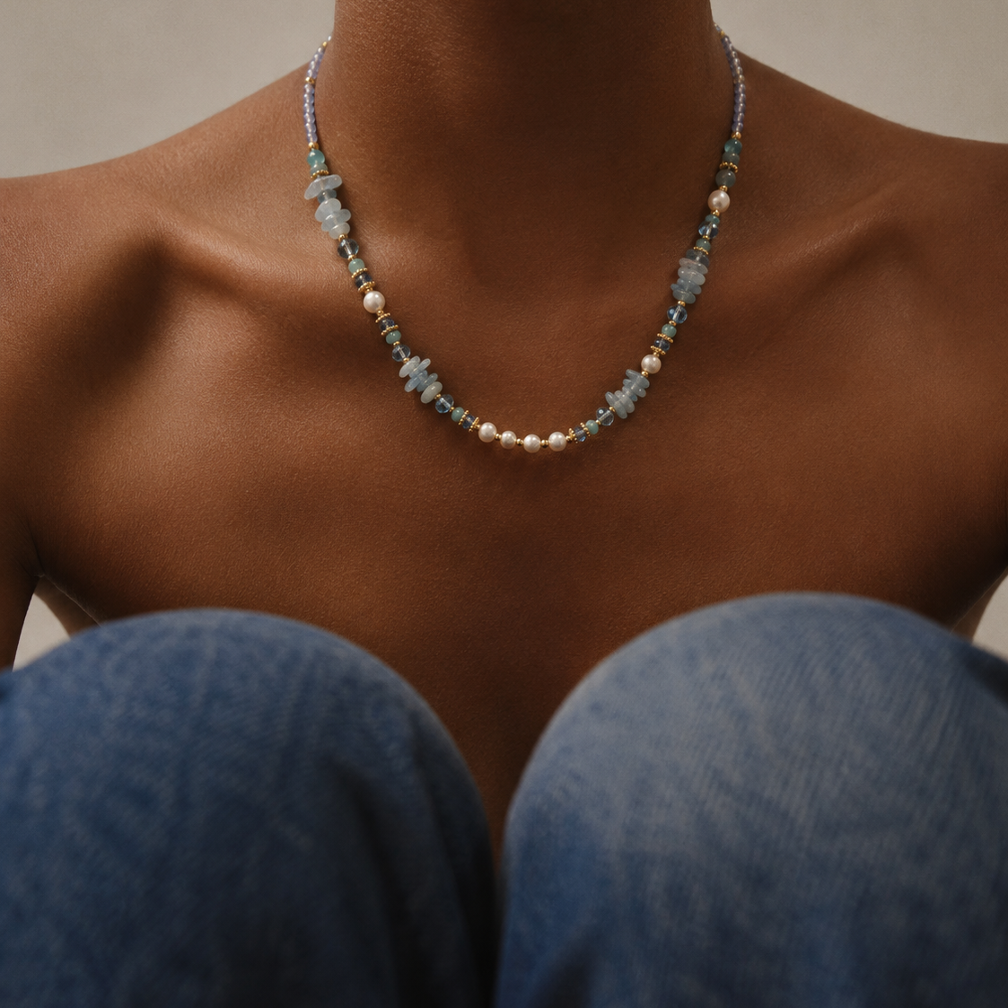Necklace with blue and gold beads on a person wearing blue jeans.