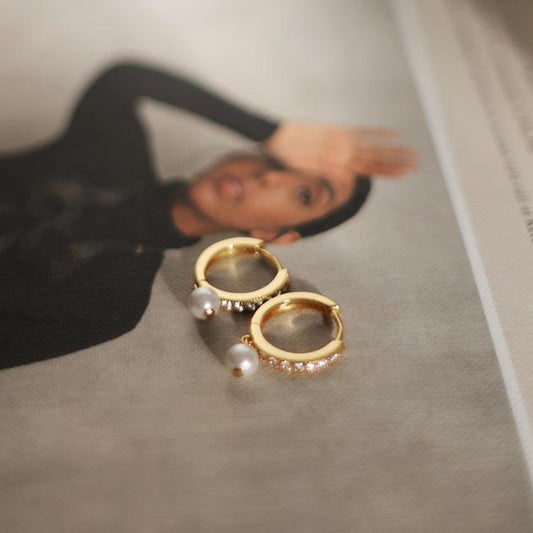 gold single pearl hoops lying on a fashion magazine