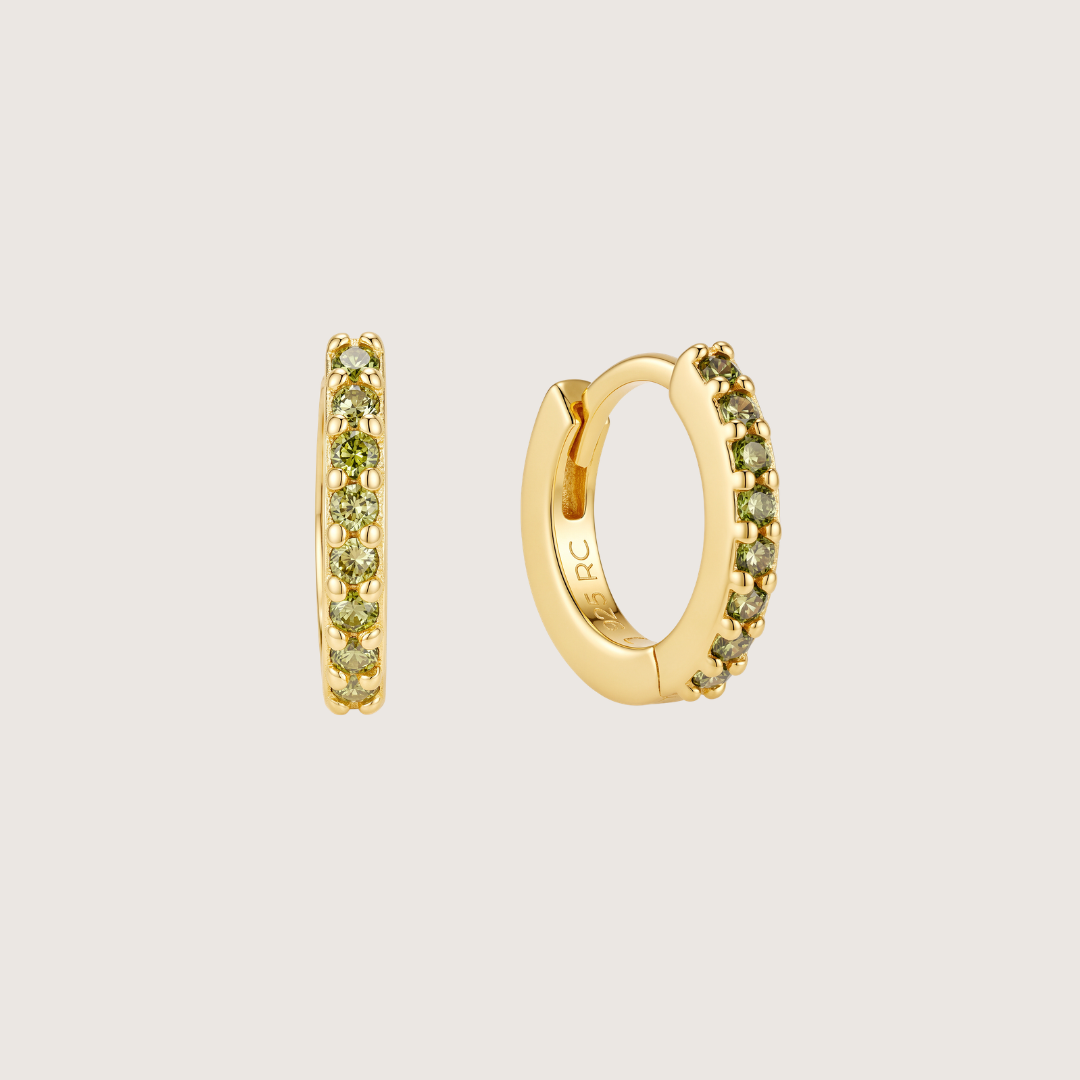 A pair of gold huggie hoop earrings with a row of small green gemstones, shown from both front and side angles on a light gray background.