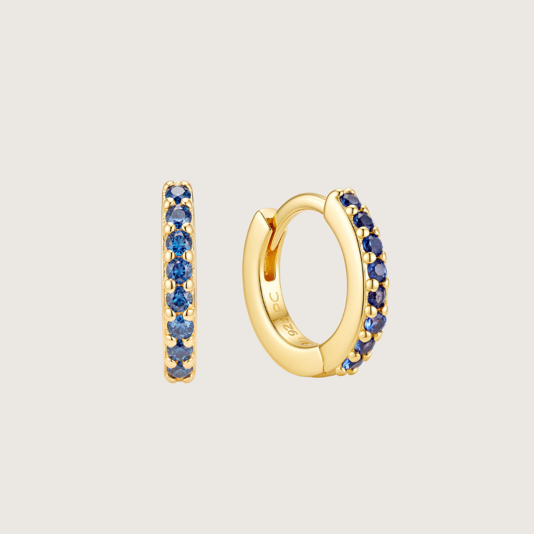 Gold huggie hoop earrings with a row of round blue gemstones, shown from both front and side views on a light gray background.