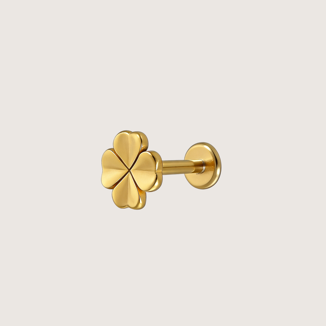 A gold four-leaf clover stud earring shown from a side angle against a solid light gray background.