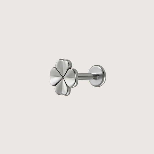 A silver four-leaf clover stud earring with a polished finish, shown from a three-quarter angle on a light beige background.
