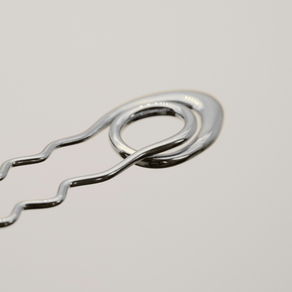 A close-up of a shiny silver metal bobby pin on a light gray background.