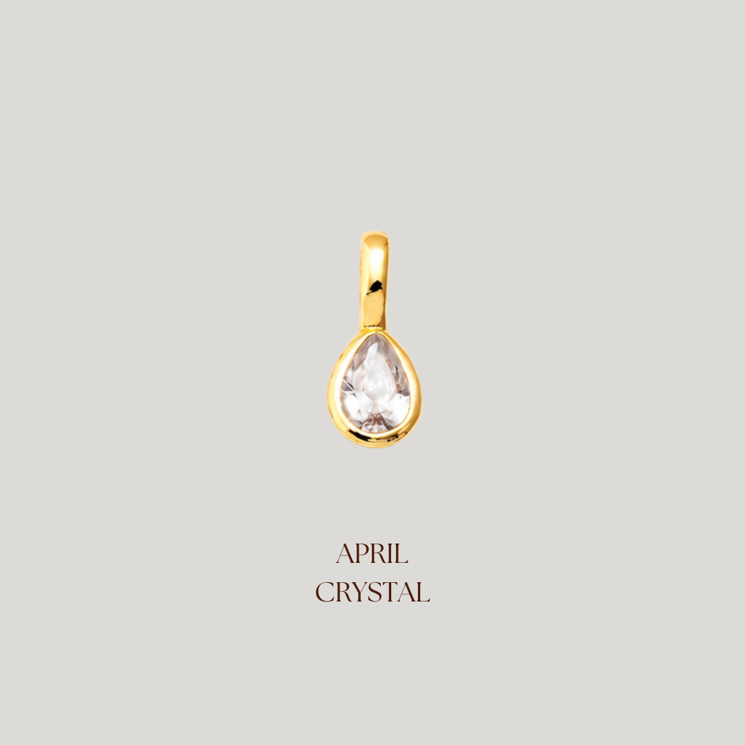 Gold teardrop-shaped pendant with a clear gemstone on a light gray background, labeled 'April Crystal'.