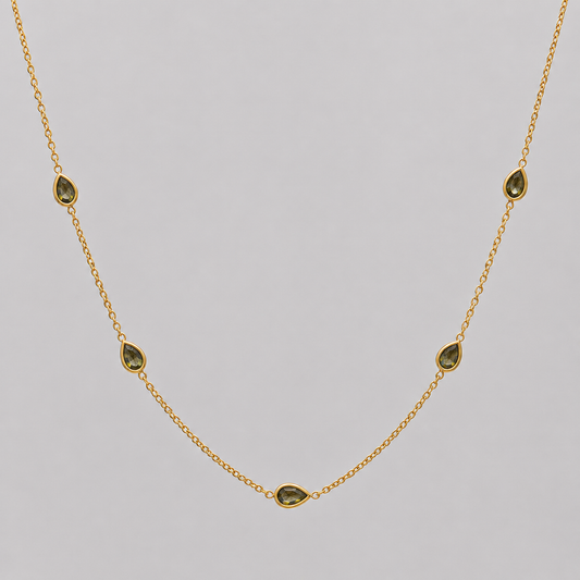 Gold necklace with green gemstones on a grey background