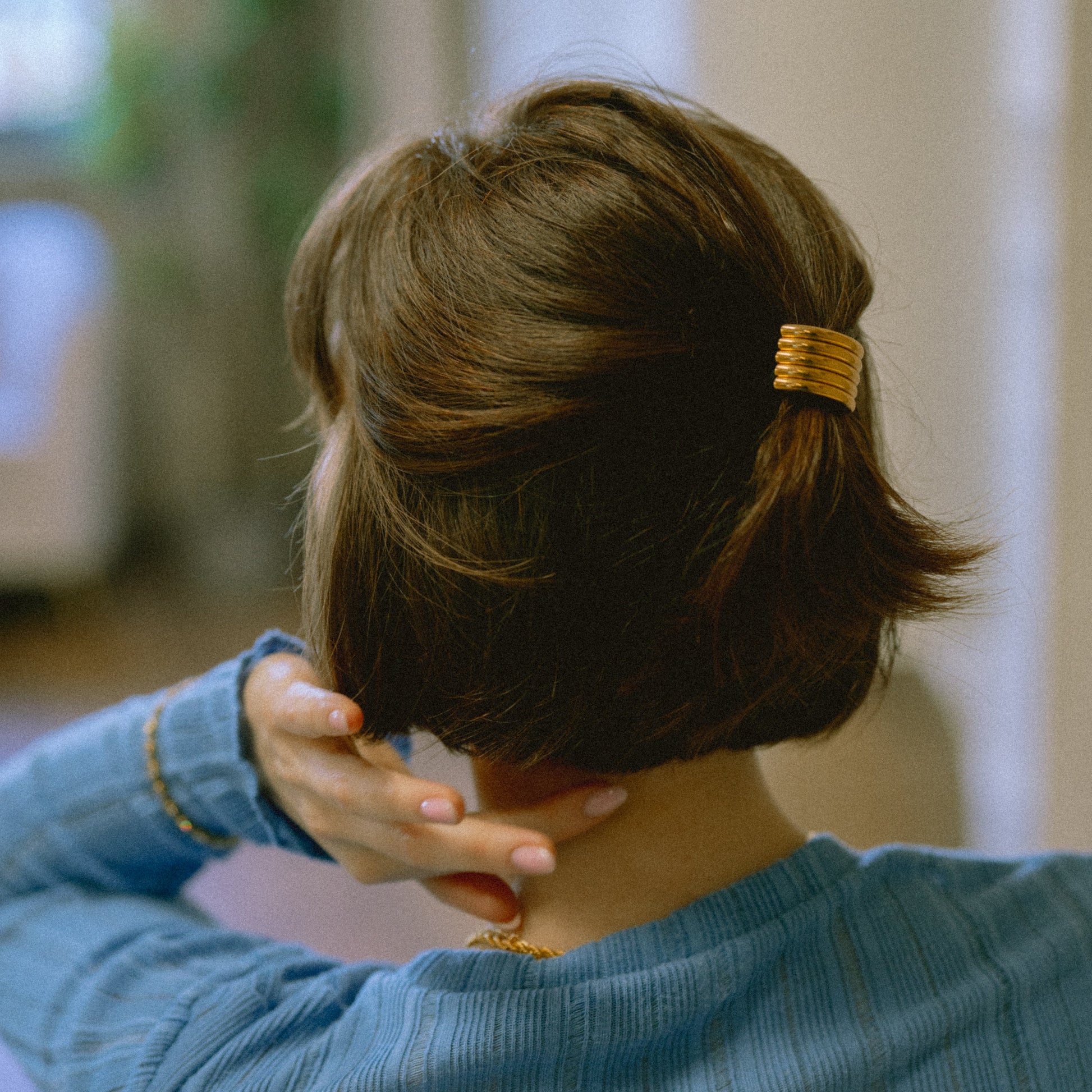 Person with a gold hair clip in their hair, wearing a blue shirt indoors.