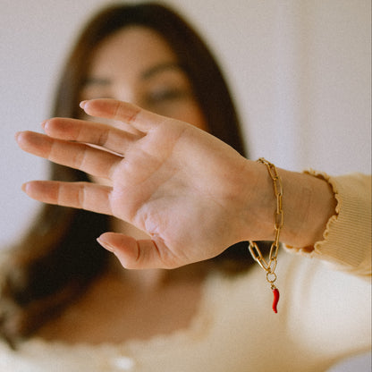 Woman wearing a gold bracelet with a red charm, holding her hand out in front of her face.