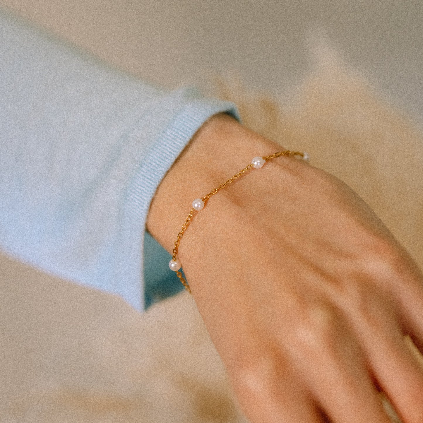 Gold bracelet with pearls on a wrist against a neutral background