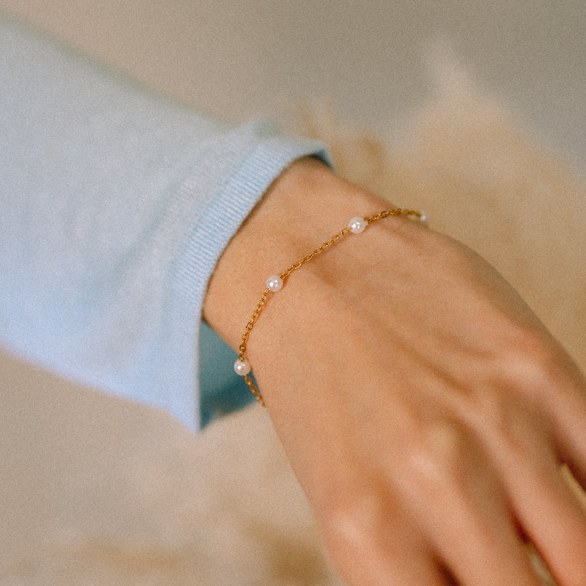 Gold bracelet with pearls on a wrist against a neutral background