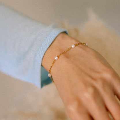 Gold bracelet with pearls on a wrist against a neutral background