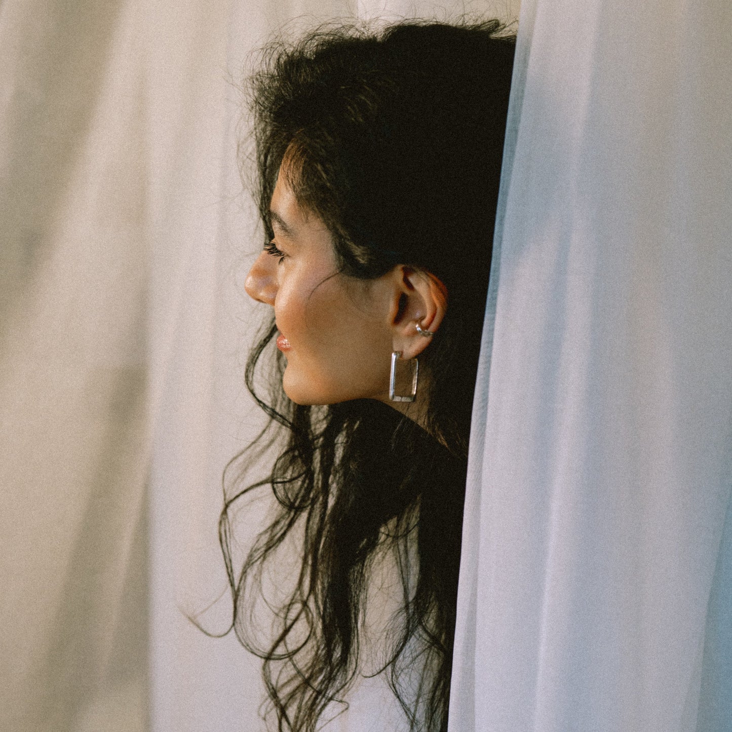 Woman peeking through sheer curtains with a soft focus