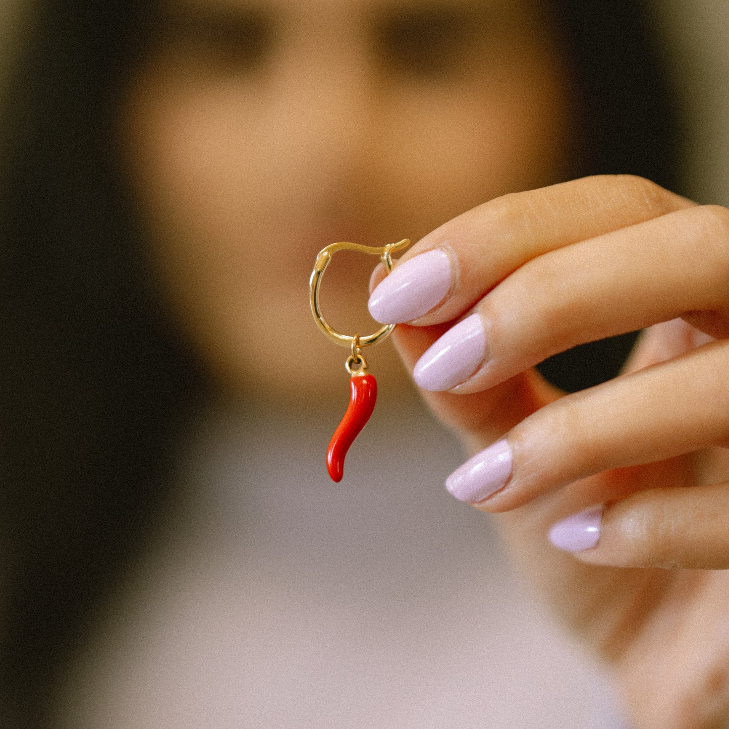 Hand holding a red chili pepper-shaped earring with a blurred background