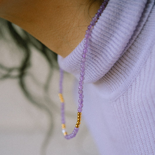 Close-up of a person wearing a light purple sweater with a beaded necklace.