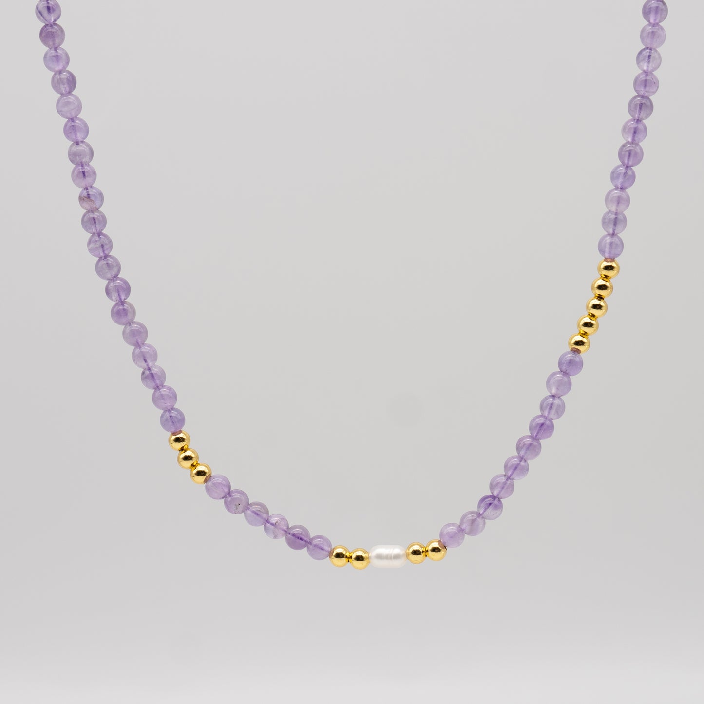 Necklace with purple beads and gold accents on a light gray background