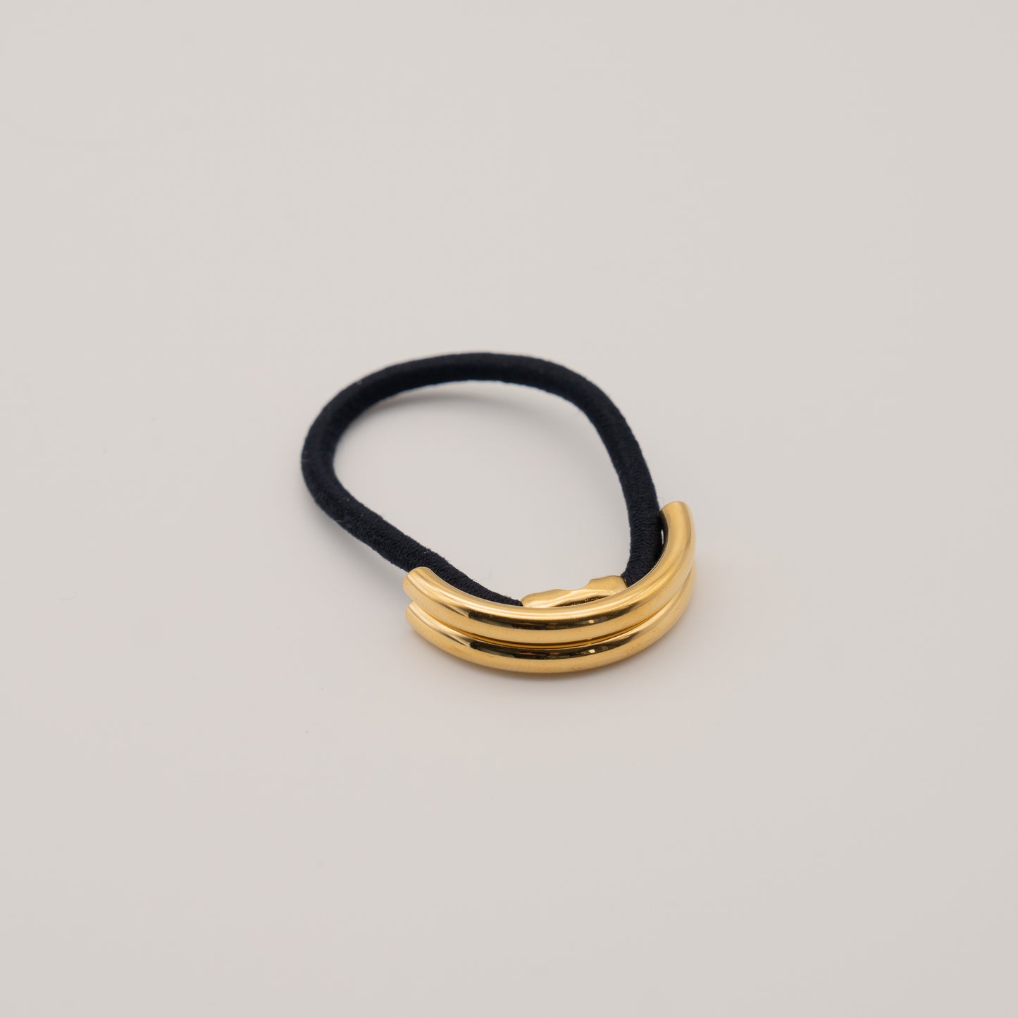 A gold double arch ponytail cuff on a black elastic band, displayed against a neutral background.