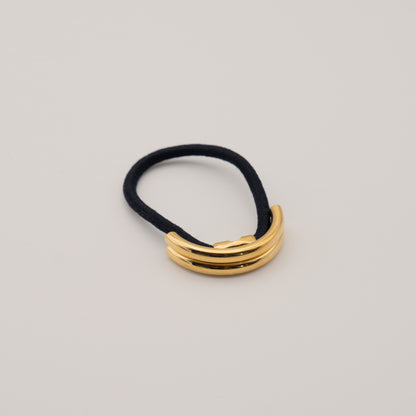 A gold double arch ponytail cuff on a black elastic band, displayed against a neutral background.