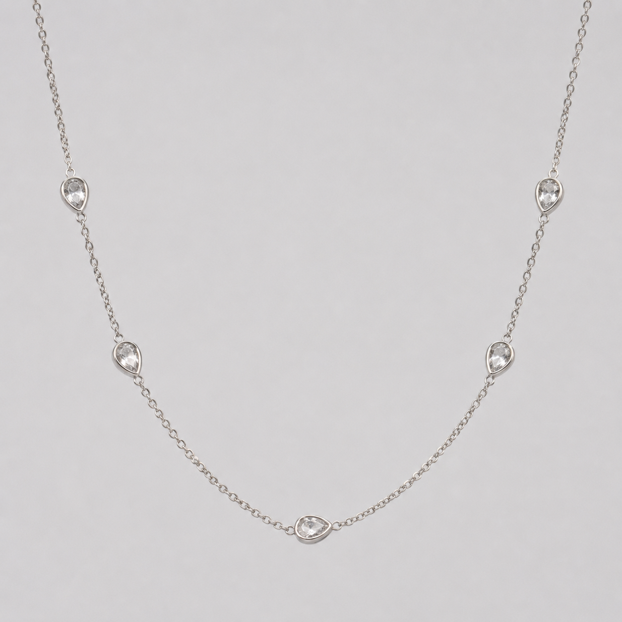 Delicate silver necklace with small teadrop-shaped diamonds on a light grey background