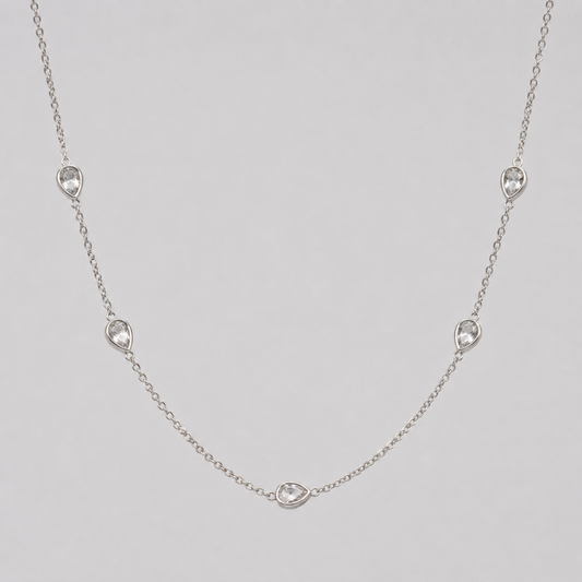 Delicate silver necklace with small teadrop-shaped diamonds on a light grey background