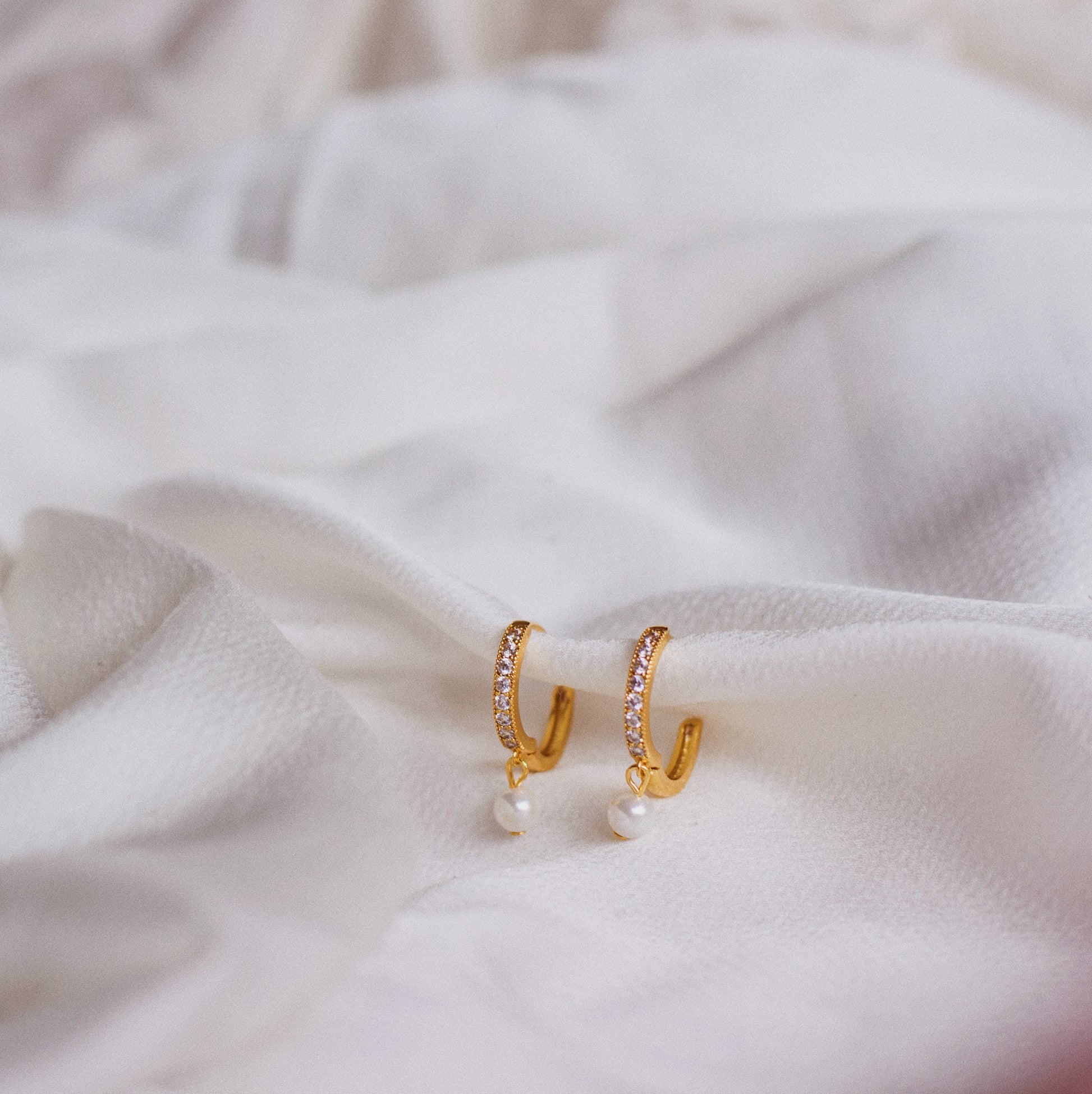 Gold plated single pearl hoops lying on silk white satin fabric